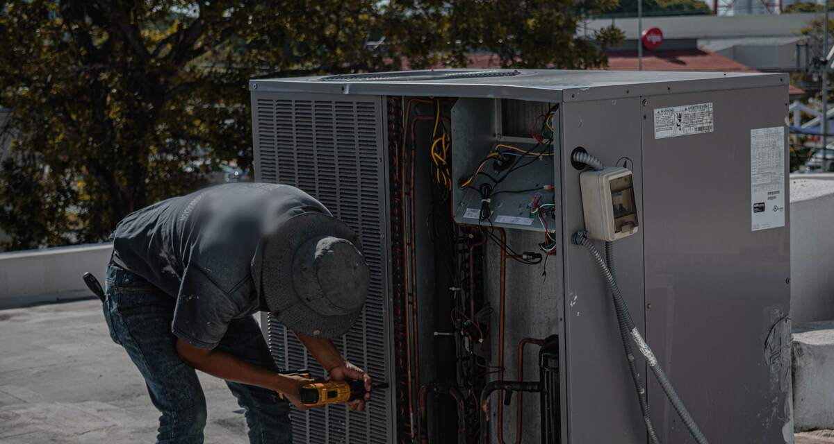 HVAC technician with a drill servicing an opened rooftop air-conditioning unit